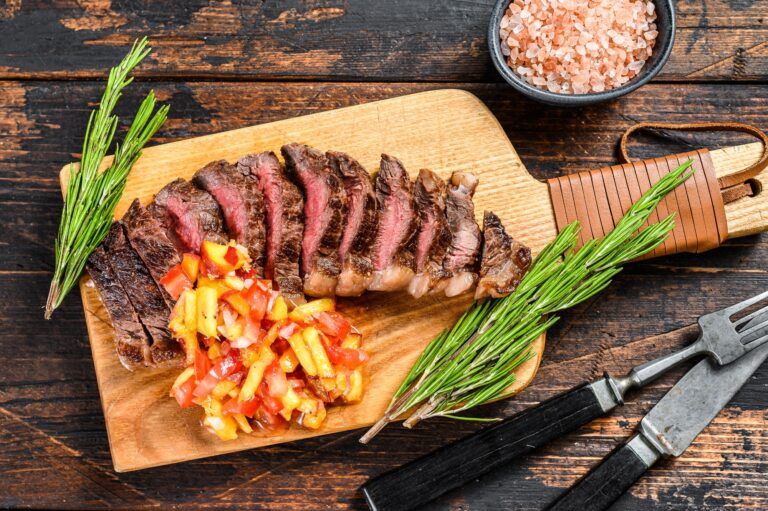 Grilled top sirloin cap or picanha steak on a cutting board with herbs.